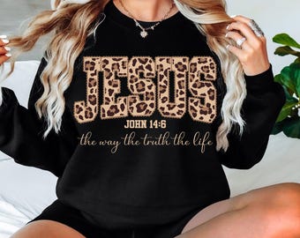 May include: Black sweatshirt with the word "JESUS" in a leopard print design. Below the word "JESUS" is the text "JOHN 14:6" and the phrase "the way the truth the life" in a script font.