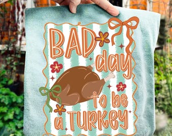 May include: A teal and white striped decorative pillow with the text "BAD day to be a TURKEY" in orange and white. The pillow features a cartoon turkey and floral accents, with orange and green bows.