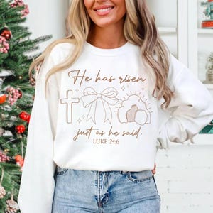 May include: White sweatshirt with a brown graphic design that says "He has risen just as he said. Luke 24:6". The graphic includes a cross, a bow, and a tomb.