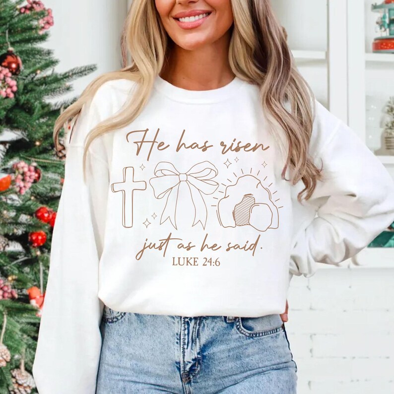 May include: White sweatshirt with a brown graphic design that says "He has risen just as he said. Luke 24:6". The graphic includes a cross, a bow, and a tomb.