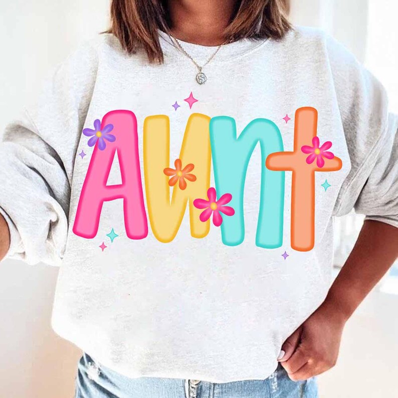 Peut inclure: Un sweat-shirt blanc avec le mot "AUNT" imprim&eacute; en lettres color&eacute;es avec des fleurs autour des lettres. Les lettres sont roses, jaunes, bleues et orange.