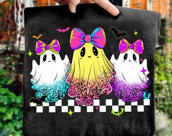 May include: Black tote bag featuring three cartoon ghosts with bows. The ghosts have colorful gradients and leopard print accents. Bats and stars decorate the top. A black and white checkered pattern is at the bottom.