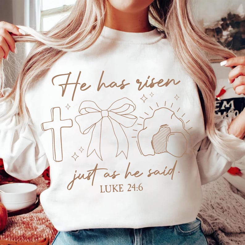 May include: White sweatshirt with a brown graphic design that says "He has risen just as he said. LUKE 24:6". The graphic includes a cross, a bow, and a tomb.