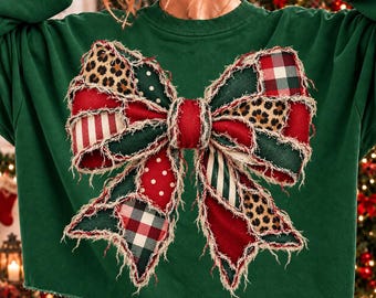 May include: A dark green long-sleeve sweatshirt featuring a large, central bow graphic made of frayed fabric patches. The bow design incorporates various patterns including leopard print, red and white stripes, red with white polka dots, and plaid.