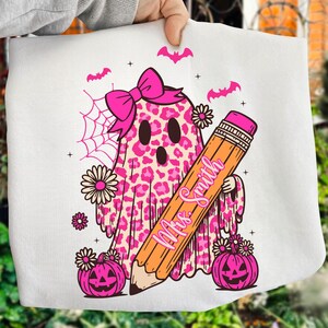 May include: White Halloween-themed design featuring a pink leopard print ghost wearing a bow, holding a pencil with "Mrs. Smith" written on it. Includes pink pumpkins, bats, spiderweb, and flowers. A fun, festive design.