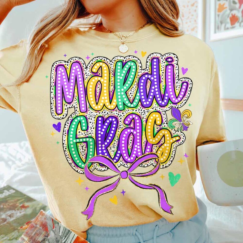 May include: A yellow t-shirt with a purple, green and yellow "Mardi Gras" graphic featuring a purple bow and hearts.