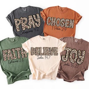 May include: Five t-shirts in different colours, each with a word in a leopard print font: PRAY, CHOSEN, FAITH, BELIEVE, and JOY. Each shirt also has a corresponding Bible verse printed below the word.