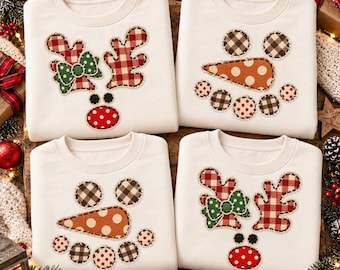 May include: Four off-white crewneck sweatshirts featuring fabric applique designs. Two sweatshirts display a reindeer face with red plaid antlers and a red polka dot nose. Two sweatshirts show a snowman face with a carrot nose and plaid circles.