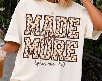 May include: An off-white short-sleeve t-shirt featuring the text MADE FOR MORE in large block letters with a brown polka dot pattern. The word for is written in a brown script font between the lines, with Ephesians 2:10 below.