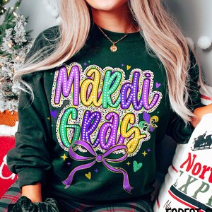 May include: Green sweatshirt with a purple, yellow and green "Mardi Gras" design with a sparkly, rhinestone-like effect. The design includes a bow and hearts.