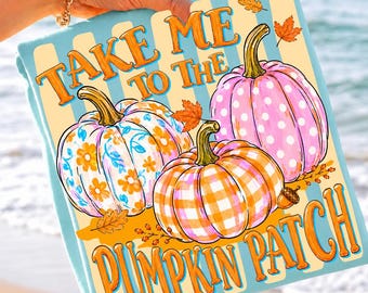 May include: A light blue blanket featuring three pumpkins with orange, pink, and white patterns including flowers, polka dots, and gingham checks. The text reads "TAKE ME TO THE PUMPKIN PATCH" in orange letters, accented by small orange autumn leaves.