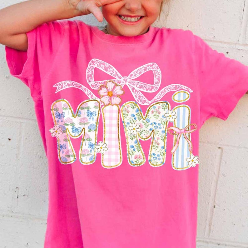 K&ouml;nnte beinhalten: Pinkes T-Shirt mit einer wei&szlig;en Schleife und dem Wort "MIMI" in bunten Patchwork-Buchstaben mit Blumen- und Gingham-Mustern.