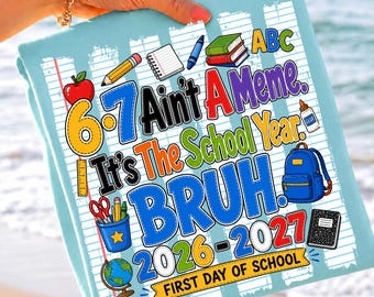 May include: A light blue t-shirt featuring a graphic print of school supplies including a red apple, pencils, a notebook, a blue backpack, and a globe. The text reads 6-7 Ain't A Meme. It's The School Year. BRUH. 2026-2027 FIRST DAY OF SCHOOL.