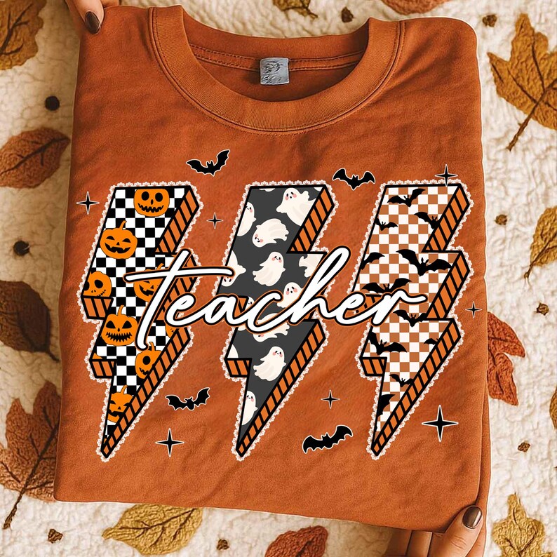 May include: An orange-brown sweatshirt featuring a Halloween-themed design. The design includes three lightning bolt shapes with checkered patterns, pumpkins, ghosts, and bats. The word "teacher" is written across the bolts in a cursive font.