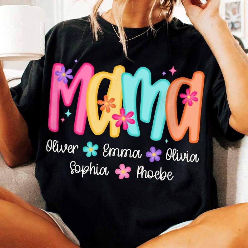 Peut inclure: T-shirt noir avec le mot "Mama" en lettres color&eacute;es et des fleurs. En dessous du mot se trouvent les noms Oliver, Emma, Sophia et Phoebe.