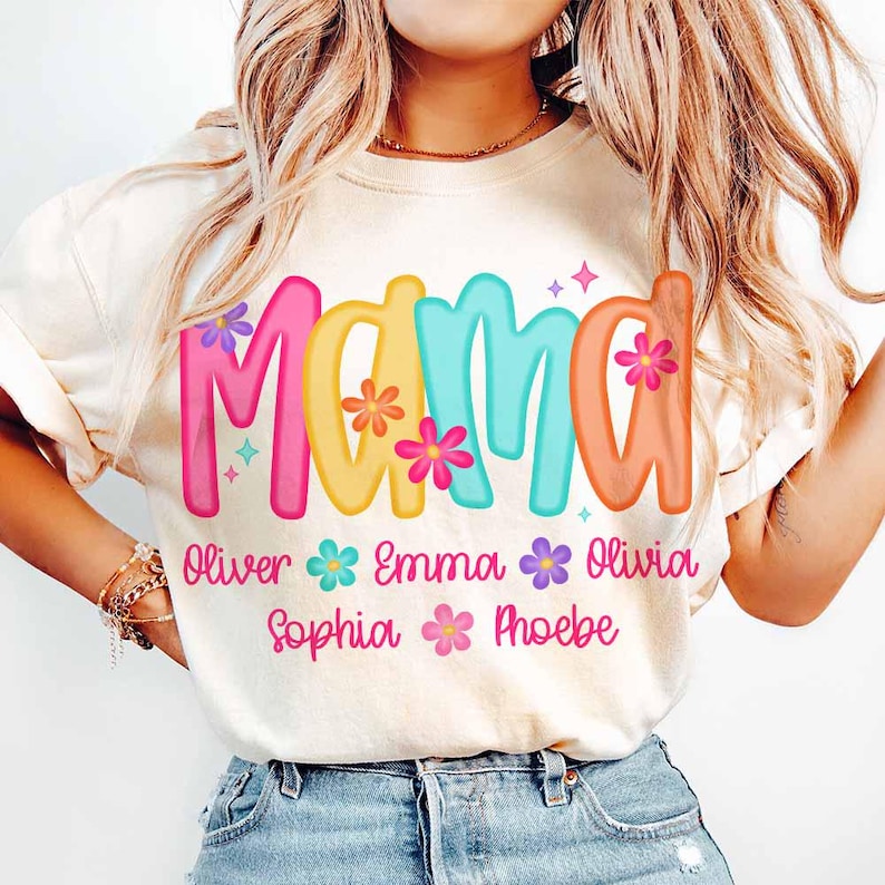 Peut inclure: Un t-shirt blanc avec le mot "Mama" en lettres color&eacute;es et des fleurs. Sous le mot se trouvent les noms "Oliver", "Emma", "Olivia", "Sophia" et "Phoebe" avec des fleurs entre chaque nom.