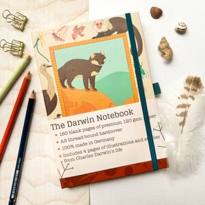 Könnte beinhalten: Ein grünes und oranges Notizbuch mit dem Text "The Darwin Notebook" und Illustrationen von Tieren. Das Notizbuch hat 160 leere Seiten aus hochwertigem 120 g/m² Papier, ist A5-faden gebunden, gebunden und 100% in Deutschland hergestellt. Es enthält 4 Seiten mit Illustrationen und Geschichten aus dem Leben von Charles Darwin.