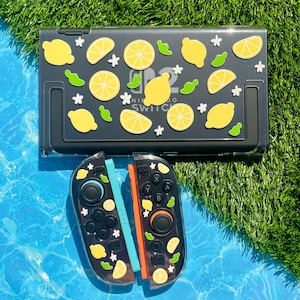 May include: A black Nintendo Switch case and controller set decorated with yellow lemon and white flower stickers. The case has the text "NINTENDO SWITCH" on it. The controllers are black with blue and orange accents.