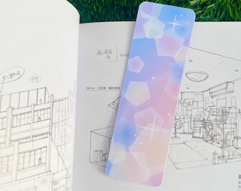 May include: A pink and blue bookmark with a glittery, abstract design. The bookmark features a pattern of overlapping geometric shapes with a subtle shimmer effect.