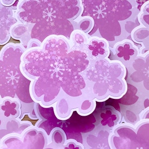 May include: A set of purple and white stickers featuring a cluster of cherry blossoms with a glittery finish. The stickers are perfect for adding a touch of whimsy to journals, laptops, or water bottles.