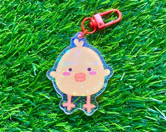 May include: A yellow chick keychain with glitter and a red metal ring. The chick has a cute face with pink cheeks and a red beak.