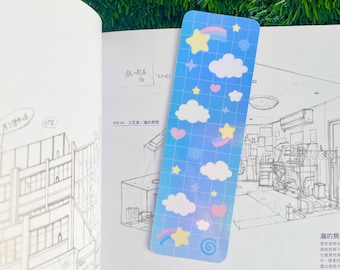 May include: A blue and pink holographic bookmark featuring a rainbow, stars, and clouds. The bookmark has a grid pattern and is decorated with hearts and swirls.