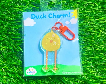 May include: A yellow duck charm with glitter and a red metal key chain. The charm is packaged on a blue and white card with the text "Duck Charm!" and "Chu Charms" on it.