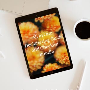 May include: A black tablet displaying the text All In One Decluttering Guide and Checklist Bundle over a blurred orange floral background. Below the tablet, the text downloadable pdf is written in a black script font on a white surface.