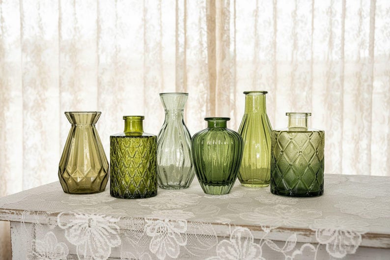 May include: A collection of six green glass vases in various shapes and sizes. The set includes vessels with geometric diamond patterns, vertical fluting, and smooth rounded silhouettes, all featuring translucent olive and emerald green glass.