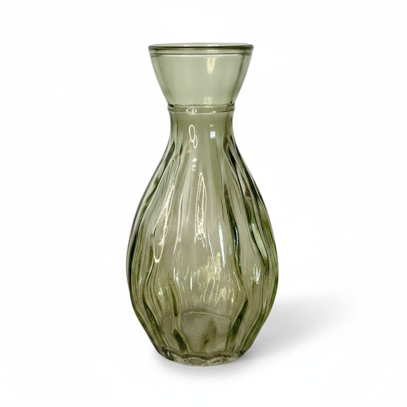 May include: A translucent sage green glass vase with a bulbous body and a flared rim. The exterior surface features a series of vertical, undulating ridges that create a rippled texture around the entire circumference of the glass vessel.