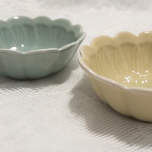 May include: Two ceramic bowls with a scalloped edge. One bowl is a pale green, the other is a soft yellow. Both bowls have a white trim and a petal-like design on the interior.