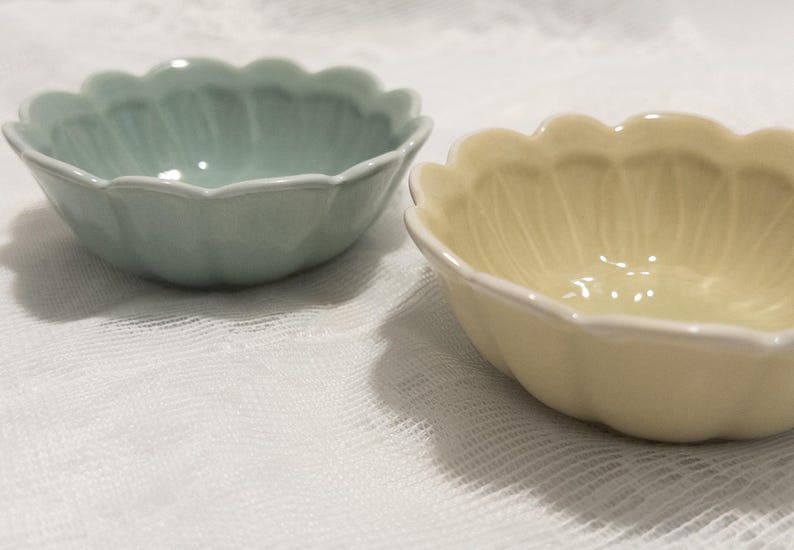 May include: Two ceramic bowls with a scalloped edge. One bowl is a pale green, the other is a soft yellow. Both bowls have a white trim and a petal-like design on the interior.