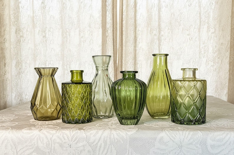 May include: A collection of six glass vases in various shades of green. The set includes vessels with geometric diamond patterns, vertical ribbed textures, and smooth tapered silhouettes, all featuring narrow openings and transparent glass construction.
