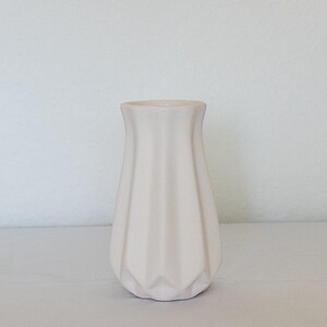 Pu&ograve; includere: Un piccolo vaso in ceramica bianco sporco con un design geometrico. Il vaso ha una parte superiore svasata e un corpo strutturato e scanalato. Il vaso &egrave; alto circa 15 cm ed &egrave; adatto per esporre fiori o come elemento decorativo.