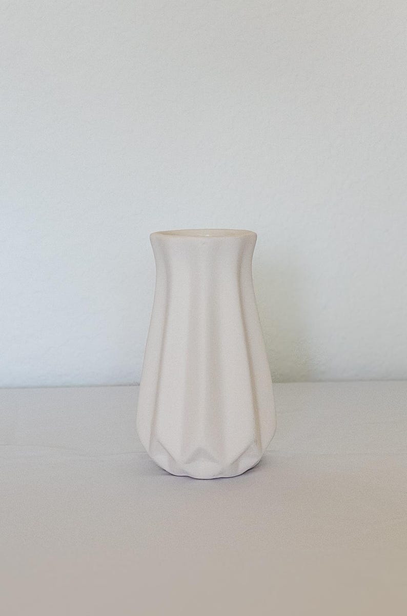 Pu&ograve; includere: Un piccolo vaso in ceramica bianco sporco con un design geometrico. Il vaso ha una parte superiore svasata e un corpo strutturato e scanalato. Il vaso &egrave; alto circa 15 cm ed &egrave; adatto per esporre fiori o come elemento decorativo.