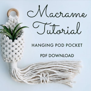May include: A white macrame hanging pod pocket with a small green plant inside. The macrame is made with a thick white cord and has a wooden ring at the top. The text "Macrame Tutorial" is written in cursive above the pod pocket. The text "Hanging Pod Pocket" is written below the pod pocket. The text "PDF Download" is written below the text "Hanging Pod Pocket".