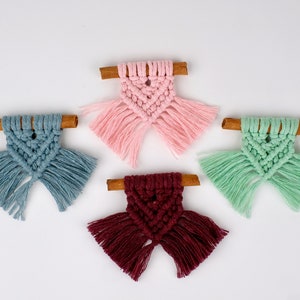May include: Four small macrame ornaments with cinnamon sticks. The ornaments are in pink, blue, green, and burgundy.