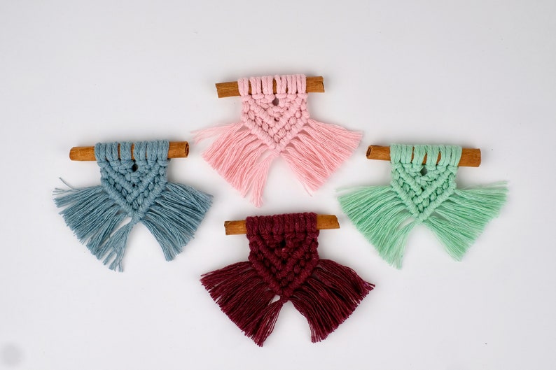May include: Four small macrame ornaments with cinnamon sticks. The ornaments are in pink, blue, green, and burgundy.