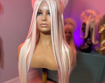May include: A long, straight blonde wig with thin, burgundy streaks. The wig is styled with a high bouffant and a side part. The wig is on a mannequin head.