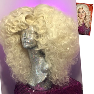 May include: A large, blonde wig with big, curly, voluminous hair. The wig is styled in a bouffant with long, flowing curls. The wig is on a mannequin head with a silver glitter finish.