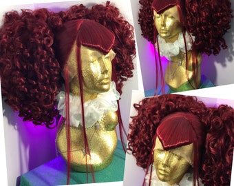 May include: A red wig with long straight bangs and two curly pigtails. The wig is on a mannequin head with a white lace collar.