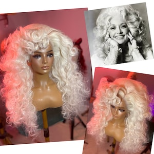 May include: A long, white, curly wig with a side part. The wig is styled in a large, voluminous shape, similar to the hairstyle of a famous country music singer.
