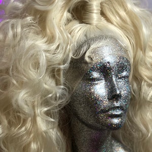 May include: A blonde wig with long, curly hair styled in a high ponytail. The wig is on a mannequin head with a silver glitter finish.