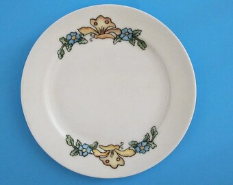 May include: A white ceramic plate with a floral design. The plate has a yellow butterfly with blue flowers and green leaves around the edge.