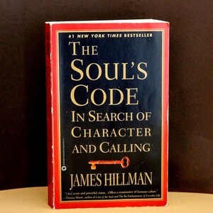 May include: A hardcover book titled "The Soul's Code" by James Hillman. The cover is black with gold lettering and a red border. The book is a New York Times bestseller and features a key illustration.
