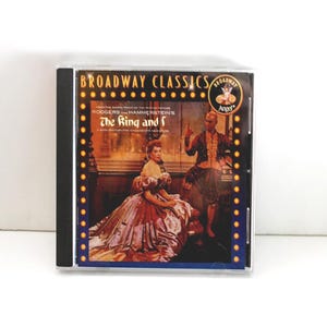 May include: A CD case featuring the Broadway Classics album "The King and I." The cover art depicts a scene from the musical with two costumed figures. The album title and artist names are prominently displayed.