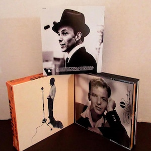 May include: A collection of Frank Sinatra album covers. The covers feature black and white images of Sinatra in various poses, including one with a fedora and another with a microphone. The album covers are in a variety of sizes and shapes.