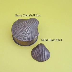 May include: A brass clamshell box and a solid brass shell are displayed on a yellow background. The box is a clamshell shape with a lid, and the shell is a smaller, standalone piece. The text "Brass Clamshell Box" and "Solid Brass Shell" are visible.