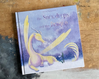 Puede incluir: Una portada de libro infantil con un fondo morado y un dragón amarillo con una flor blanca en primer plano. El título del libro es "The Snowdrops and the Dragon" de Jenna Papponetti.