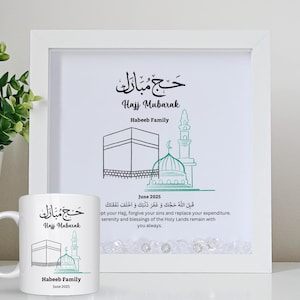 May include: A white framed print and a matching mug. The print and mug feature the text "Hajj Mubarak" in Arabic and English, along with line drawings of religious structures. The text "Habeeb Family" and "June 2025" are also included.
